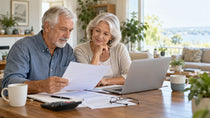 Couple de seniors comparant des documents de mutuelle santé devant un ordinateur portable.